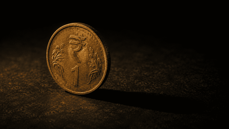 Dramatic amber-lit Indian rupee coin on dark background symbolising inflation eroding purchasing power of savings